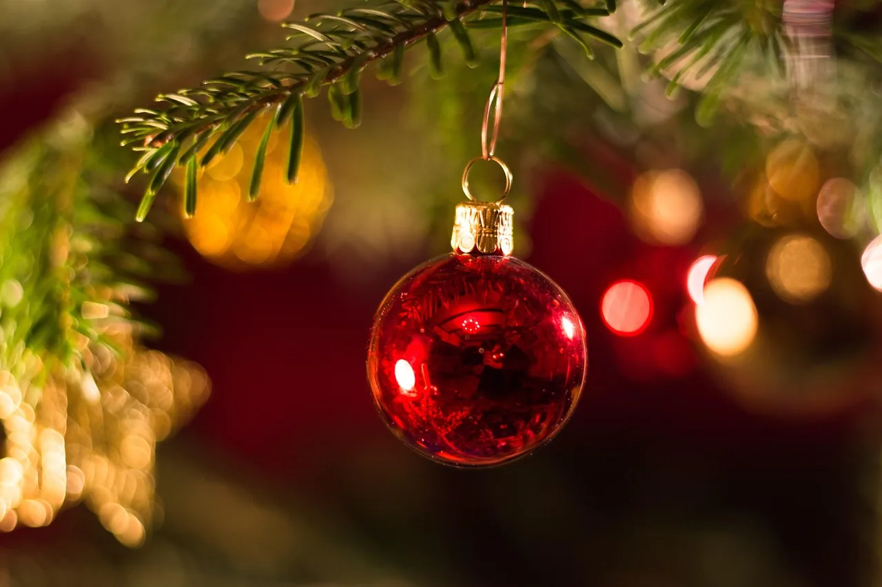 Boule de Noël rouge suspendue à une branche de sapin, lumières dorées en fond